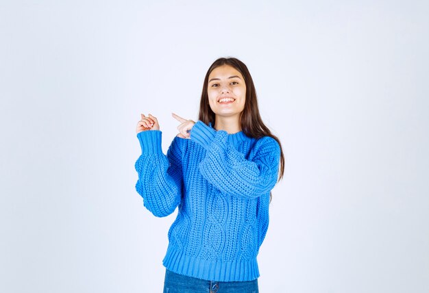 young girl model pointing away on white wall.