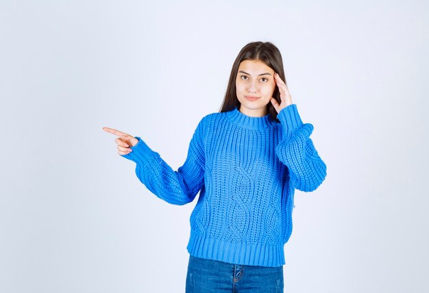 young girl model pointing away on white wall.