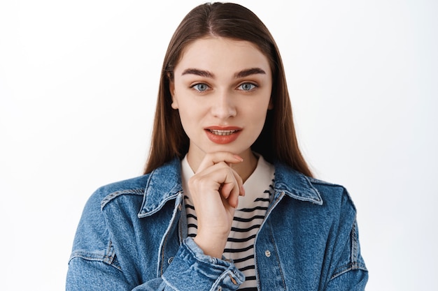 Free photo young girl model touch chin, look determined and thoughtful at front, thinking about something, pensive face, focus while making choice, standing over white wall