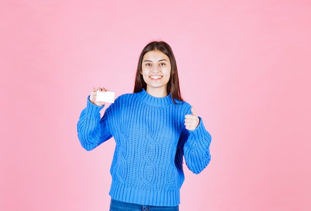 young girl model with a card showing a thumb up on pink wall.