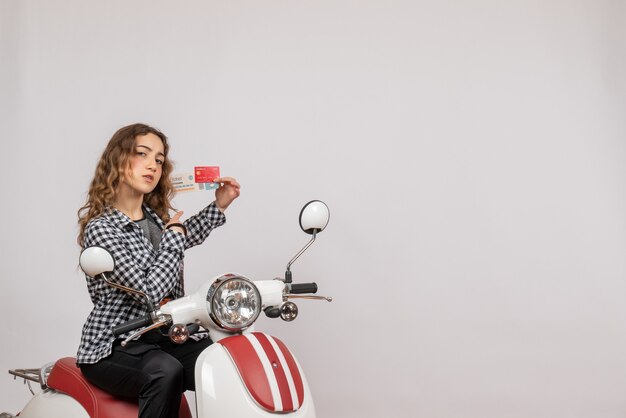 young girl on moped holding ticket and card on grey