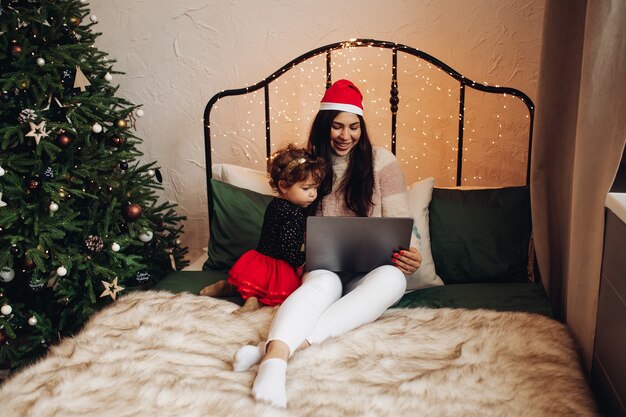 A young girl in New Year's clothes watching a TV series on the bed with a child