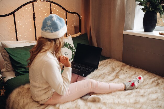 A young girl in New Year's clothes watching a TV series on the bed