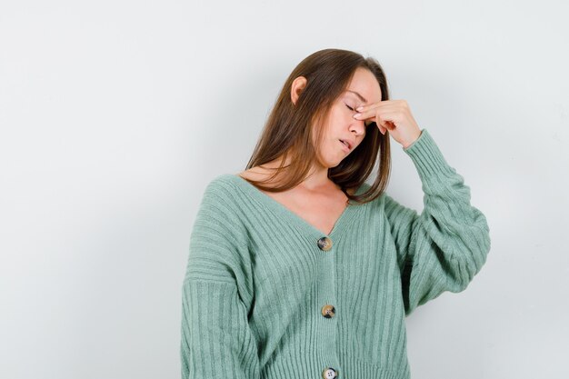 Young girl pinching bridge of nose in knitwear and looking exhausted. front view.