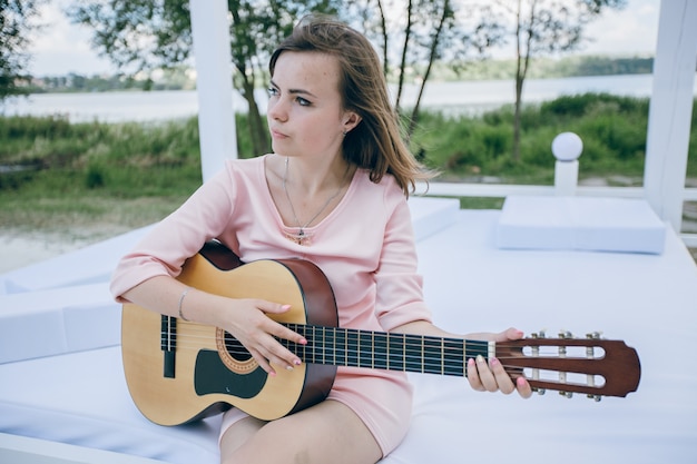 Free photo young girl in a pink dress playing a guitar