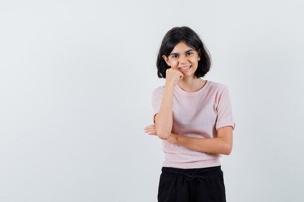 Young girl in pink t-shirt and black pants showing heavy metal gesture and pinky finger and looking happy