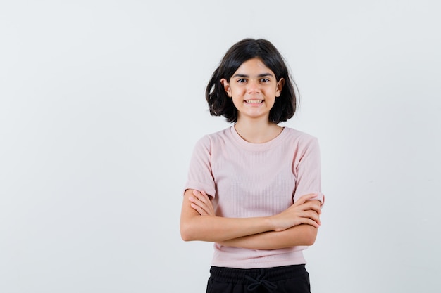 Giovane ragazza in maglietta rosa e pantaloni neri in piedi con le braccia incrociate e sorridente e guardando felice