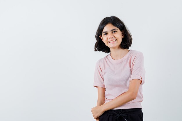 Young girl in pink t-shirt and black pants standing straight and posing at camera and looking happy