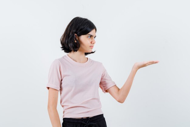 Young girl in pink t-shirt and black pants stretching hands as holding something imaginary and looking serious