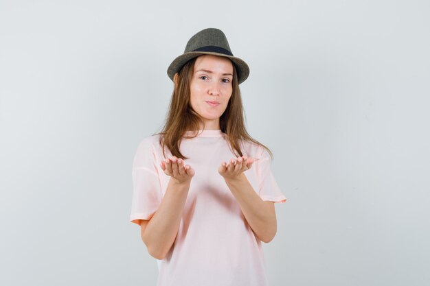 Young girl in pink t-shirt, hat pretending to hold something on palms , front view.