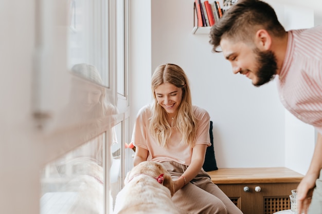 Young girl in pink t-shirt plays with dog while her boyfriend looks at them with smile.