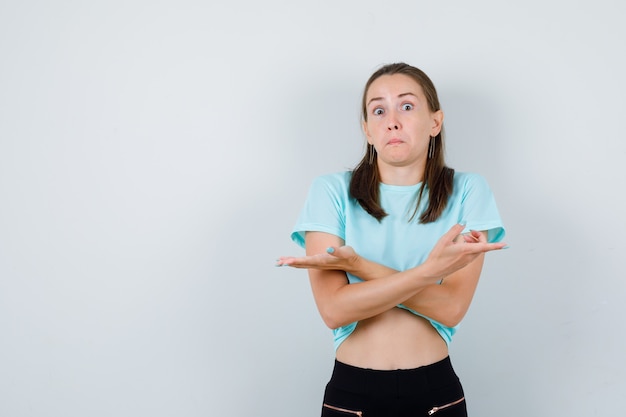 Free photo young girl pointing aside with crossed arms, bulging eyes in turquoise t-shirt, pants and looking bewildered , front view.