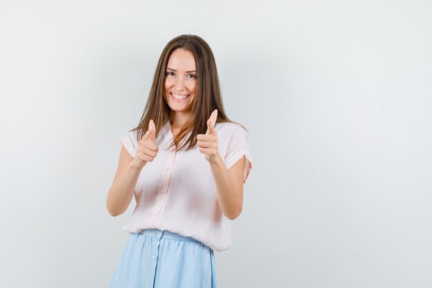 Young girl pointing at camera in t-shirt, skirt and looking jolly. front view.