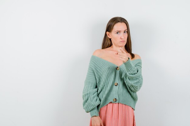 Young girl pointing at camera with index finger in knitwear, skirt and looking serious. front view.