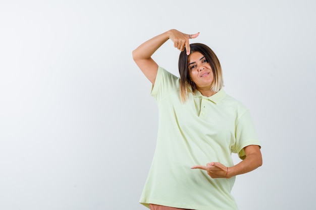 Young girl pointing down and right with index fingers in t-shirt and looking jolly , front view.