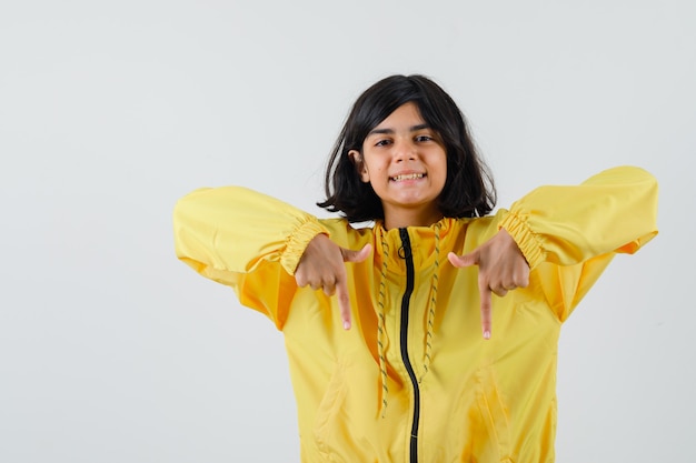 Young girl pointing down with index fingers in yellow bomber jacket and looking happy