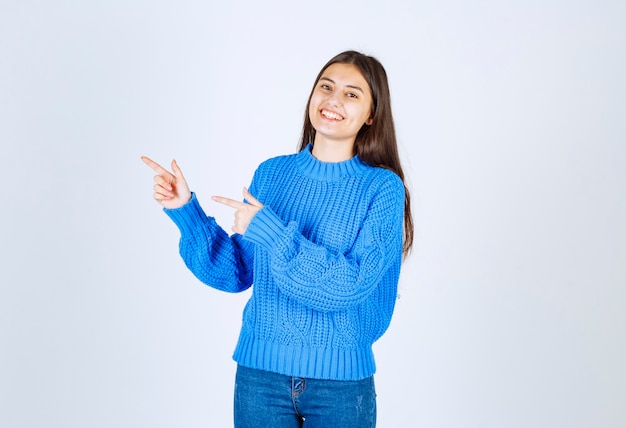 young girl pointing at her side while smiling on white.