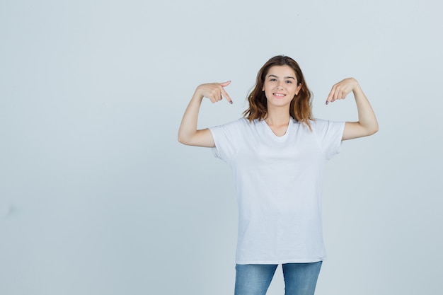 Young girl pointing herself in t-shirt, jeans and looking proud. front view.