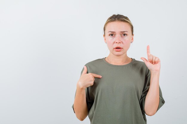 Young girl pointing herself with fingers and pointing her finger to the top on white background