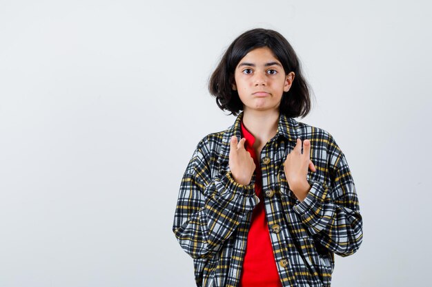 Free photo young girl pointing at herself with index fingers in checked shirt and red t-shirt and looking serious , front view.