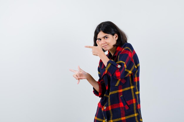 Young girl pointing left with index fingers in checked shirt and looking happy. front view.