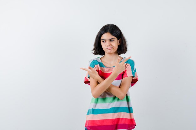 Young girl pointing opposite directions in colorful striped t-shirt and looking pensive , front view.