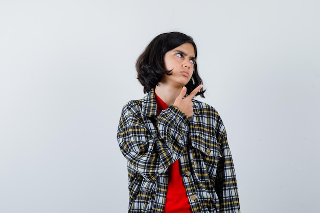 Free photo young girl pointing right with index finger in checked shirt and red t-shirt and looking serious. front view.