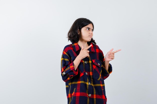 Young girl pointing right with index fingers in checked shirt and looking cute. front view.