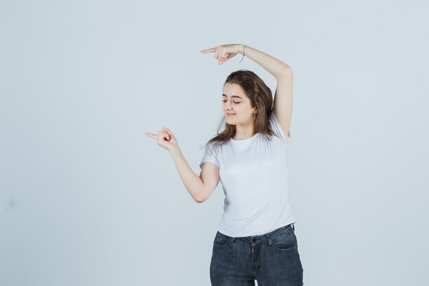 Free photo young girl pointing to the side, looking down in t-shirt, jeans and looking pleased . front view.