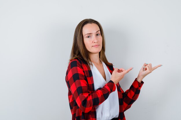 Young girl pointing to the side, standing sideways in checkered shirt, blouse and looking dissatisfied .