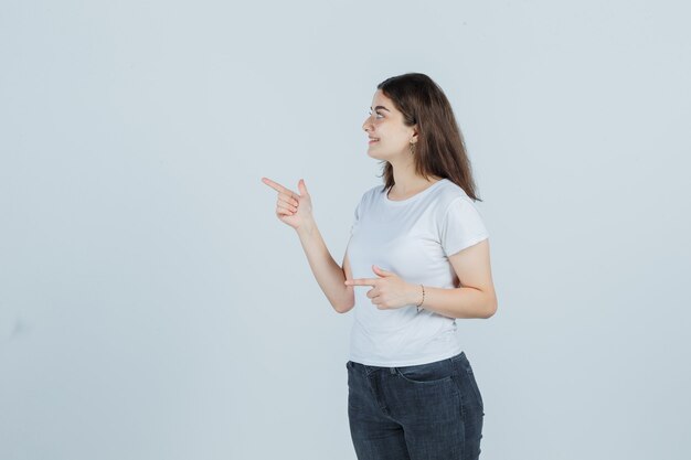 Young girl pointing to the side in t-shirt, jeans and looking sensible , front view.