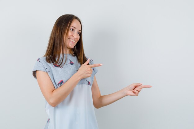 Young girl pointing to side in t-shirt and looking cheerful. front view.