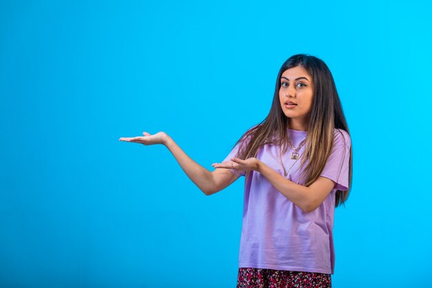 Young girl pointing at something on blue.