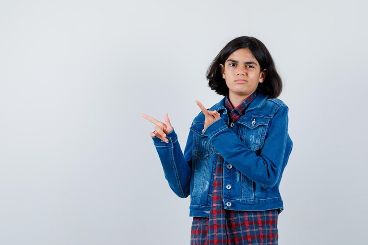 मुफ़्त फोटो young girl pointing up in checked shirt and jean jacket and looking cute. front view.