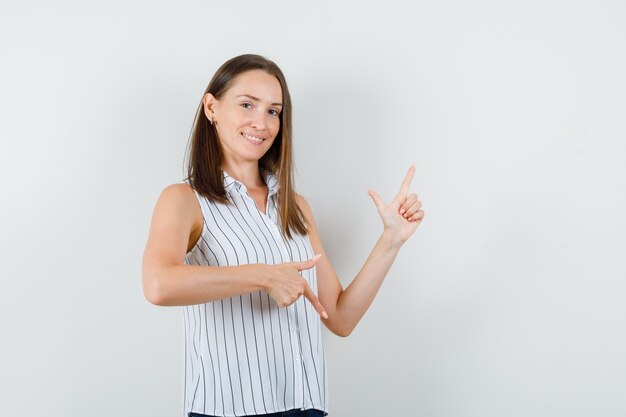 Young girl pointing up and down in t-shirt, jeans and looking glad. front view.