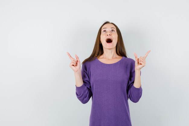 Young girl pointing up fingers in violet shirt and looking positive , front view.