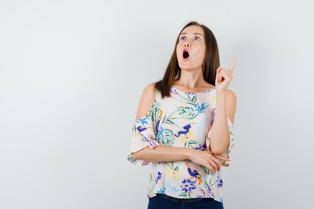 Young girl pointing up in shirt, jeans and looking astonished. front view.