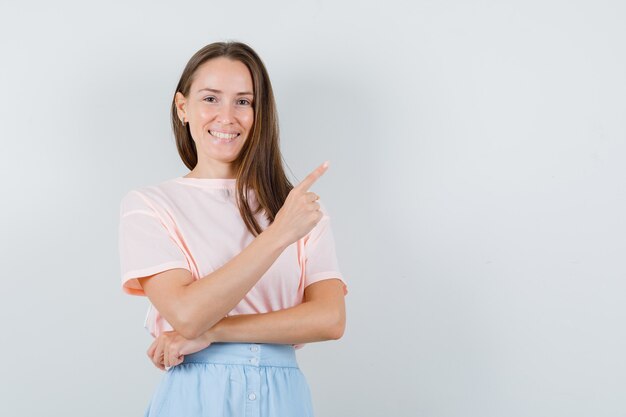 Young girl pointing up in t-shirt, skirt and looking merry. front view.