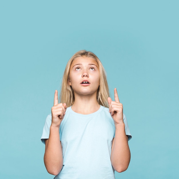 Free photo young girl pointing up with copy-space