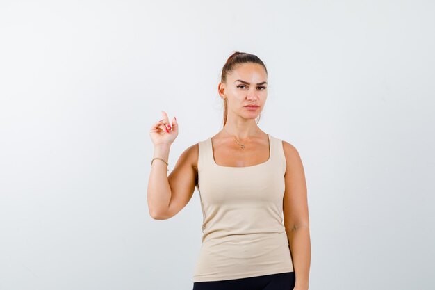 Young girl pointing up with index finger in beige top, black pants and looking serious , front view.