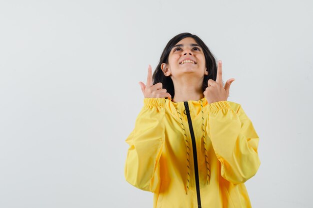 Young girl pointing up with index fingers in yellow bomber jacket and looking happy