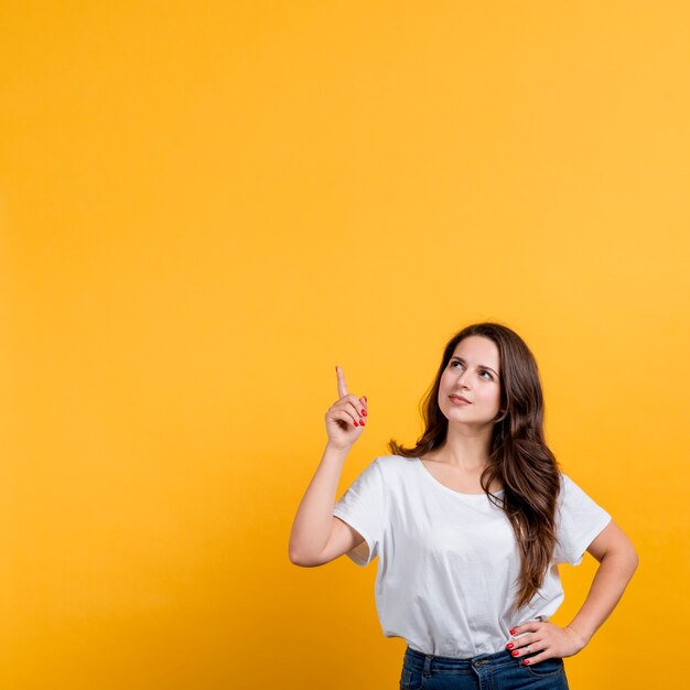 Young girl pointing up on yellow background
