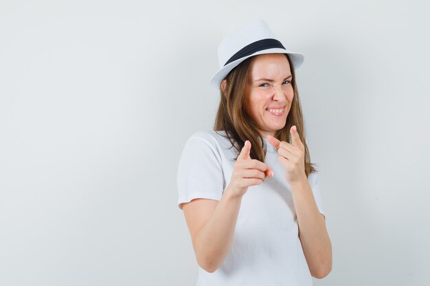 Молодая девушка указывая в белой футболке, шляпе и резвая, вид спереди.