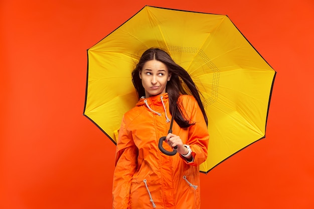 La ragazza che propone allo studio in giacca autunno isolato su rosso. emozioni negative umane. concetto del freddo. concetti di moda femminile