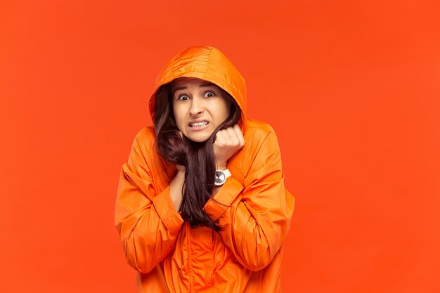 The young girl posing at studio in autumn jacket isolated on red. Human negative emotions. Concept of the cold weather. Female fashion concepts