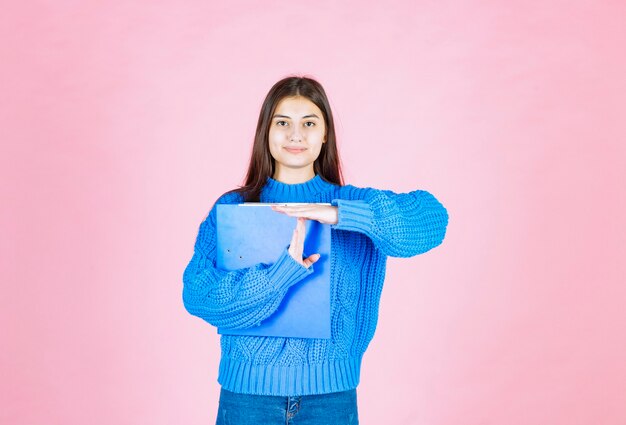 young girl posing with a blue folder on pink.