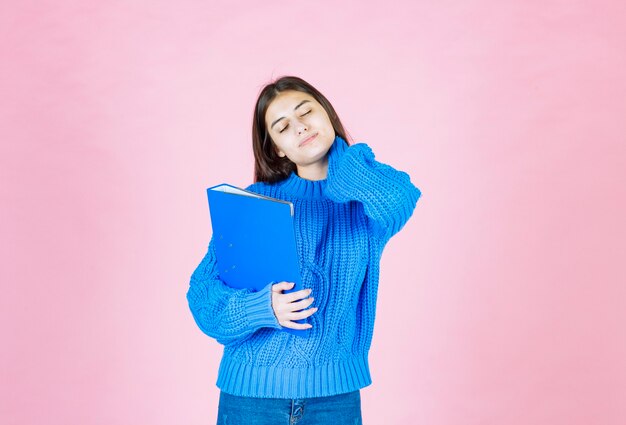 young girl posing with a blue folder on pink.