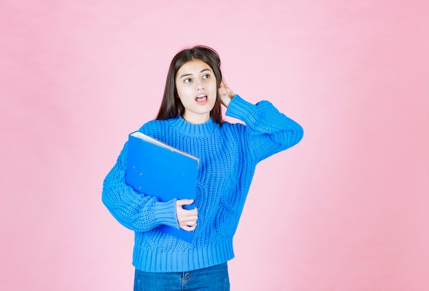 young girl posing with a blue folder on pink.