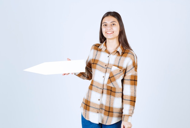 Young girl posing with empty speech arrow pointer on white wall. 