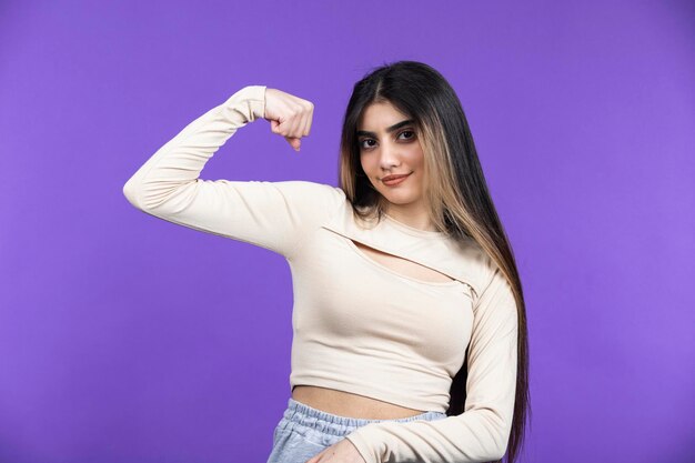 Young girl on purple background squeezing her biceps and looking at the camera